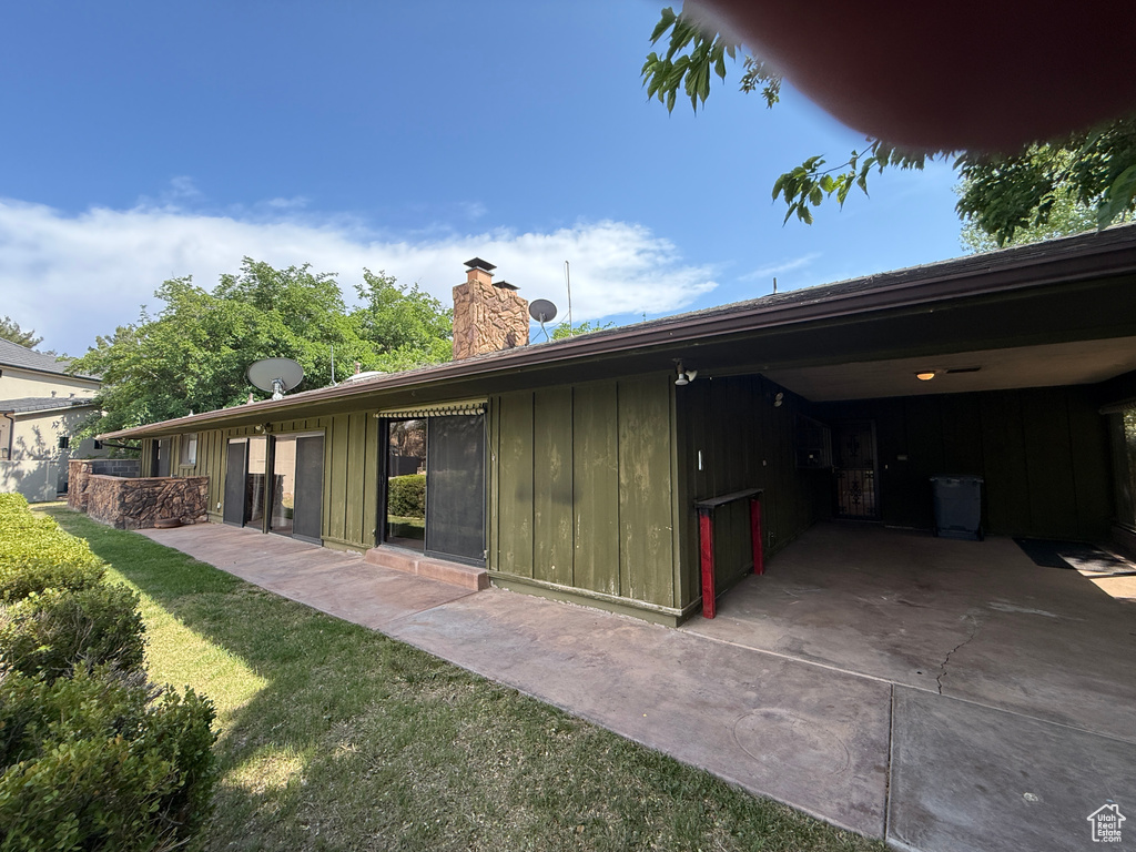 Back of property with board and batten siding, a chimney, a patio, and a lawn