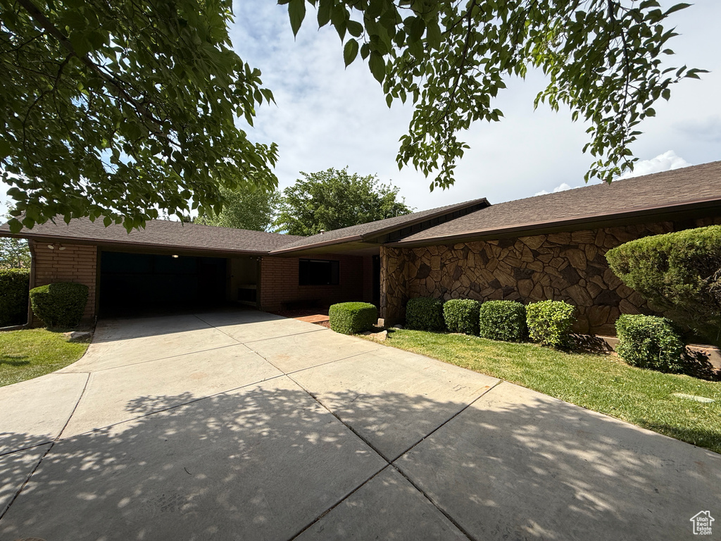 Ranch-style house with concrete driveway, an attached garage, stone siding, a front lawn, and brick siding