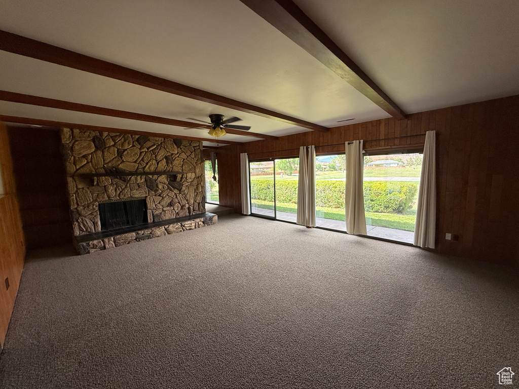 Unfurnished living room featuring beam ceiling, wood walls, carpet flooring, ceiling fan, and a stone fireplace