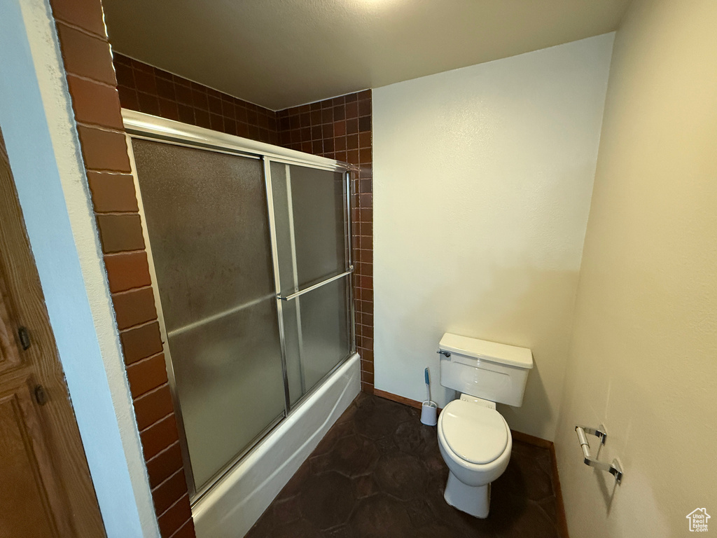 Full bath with toilet, bath / shower combo with glass door, and baseboards