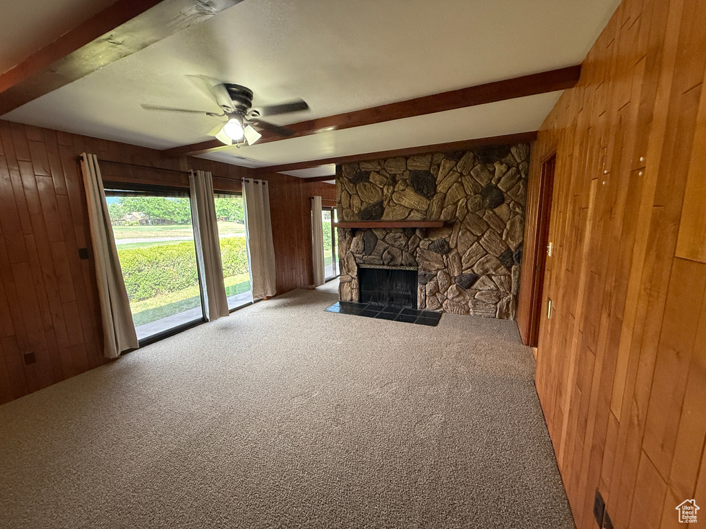 Unfurnished living room featuring beamed ceiling, wood walls, carpet, a ceiling fan, and plenty of natural light
