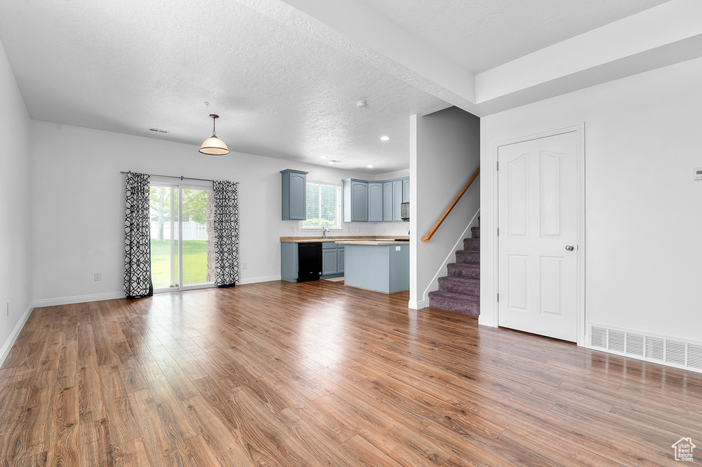 Unfurnished living room featuring light wood-style flooring, stairway, baseboards, a textured ceiling, and recessed lighting