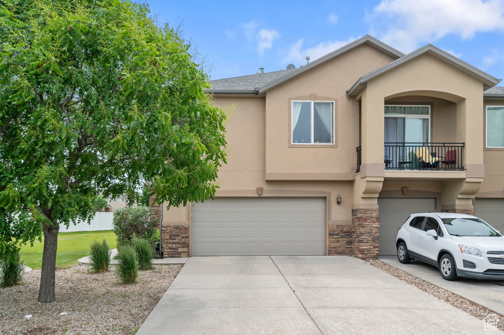 View of front facade featuring a garage, concrete driveway, stucco siding, stone siding, and a balcony