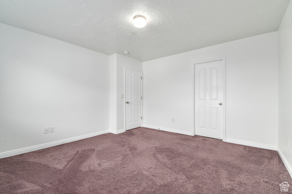 Empty room with dark carpet, a textured ceiling, and baseboards