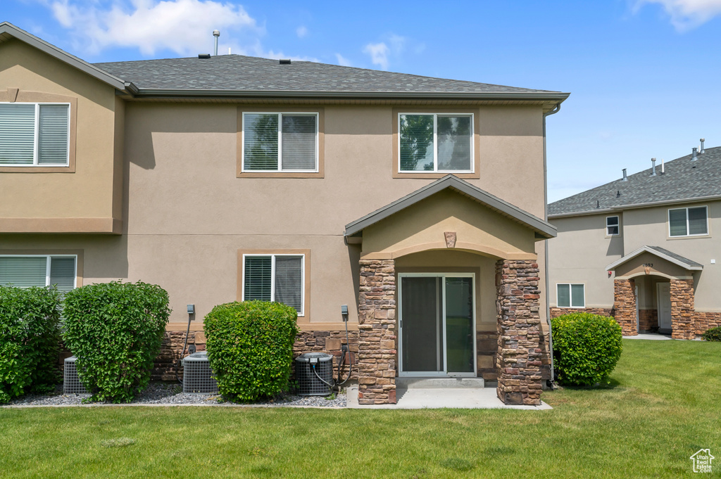 Back of house featuring stucco siding, cooling unit, and a lawn