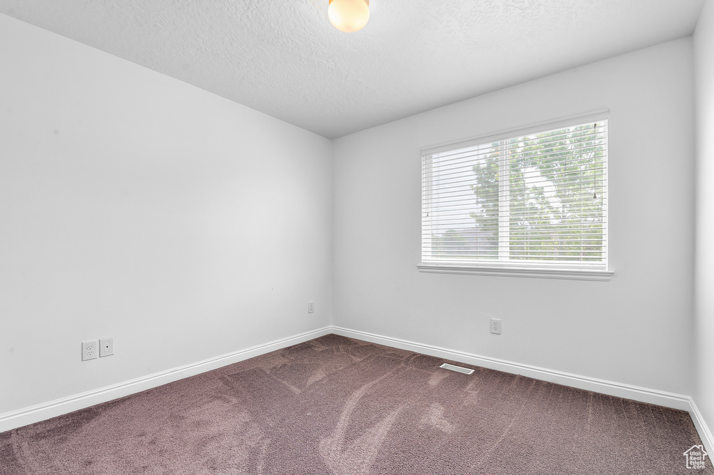 Empty room with dark colored carpet, baseboards, and a textured ceiling