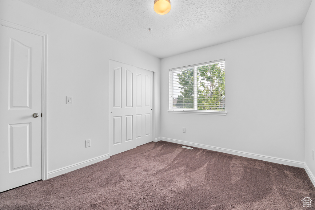 Unfurnished bedroom with carpet flooring, a textured ceiling, a closet, and baseboards