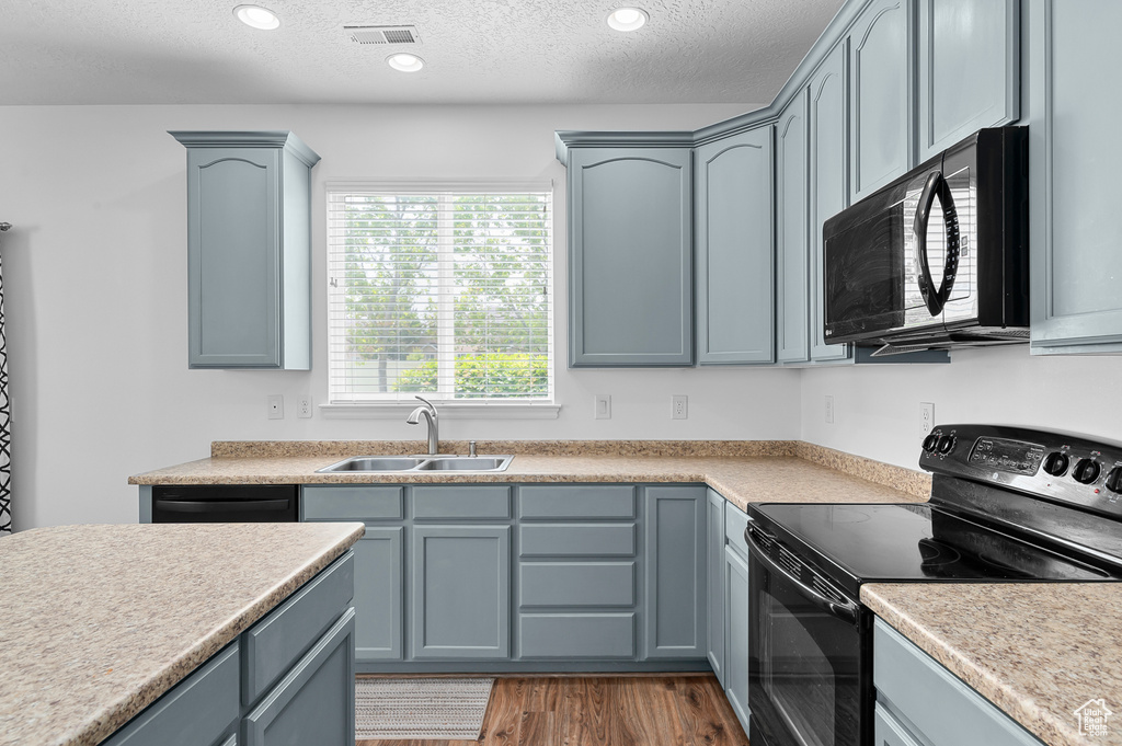 Kitchen with black appliances, a sink, wood finished floors, a textured ceiling, and light countertops