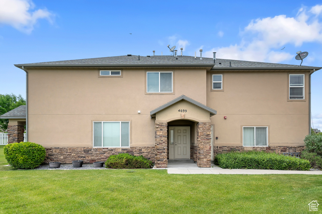 View of front of home featuring stone siding, stucco siding, a front yard, and a shingled roof