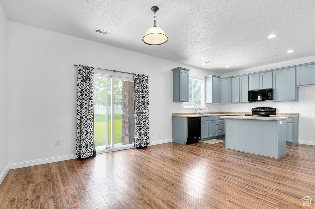 Kitchen with black appliances, a textured ceiling, light countertops, wood finished floors, and baseboards