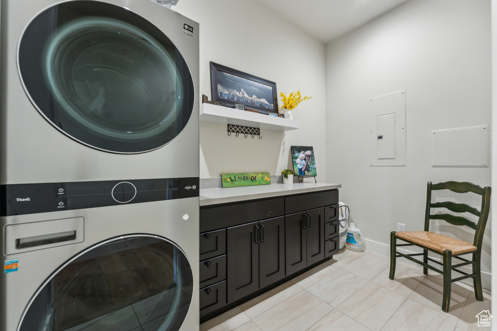 Washroom with stacked washer / drying machine, electric panel, light tile patterned flooring, cabinet space, and baseboards