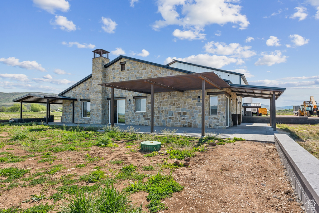 Rear view of house featuring stone siding, a patio, and a chimney