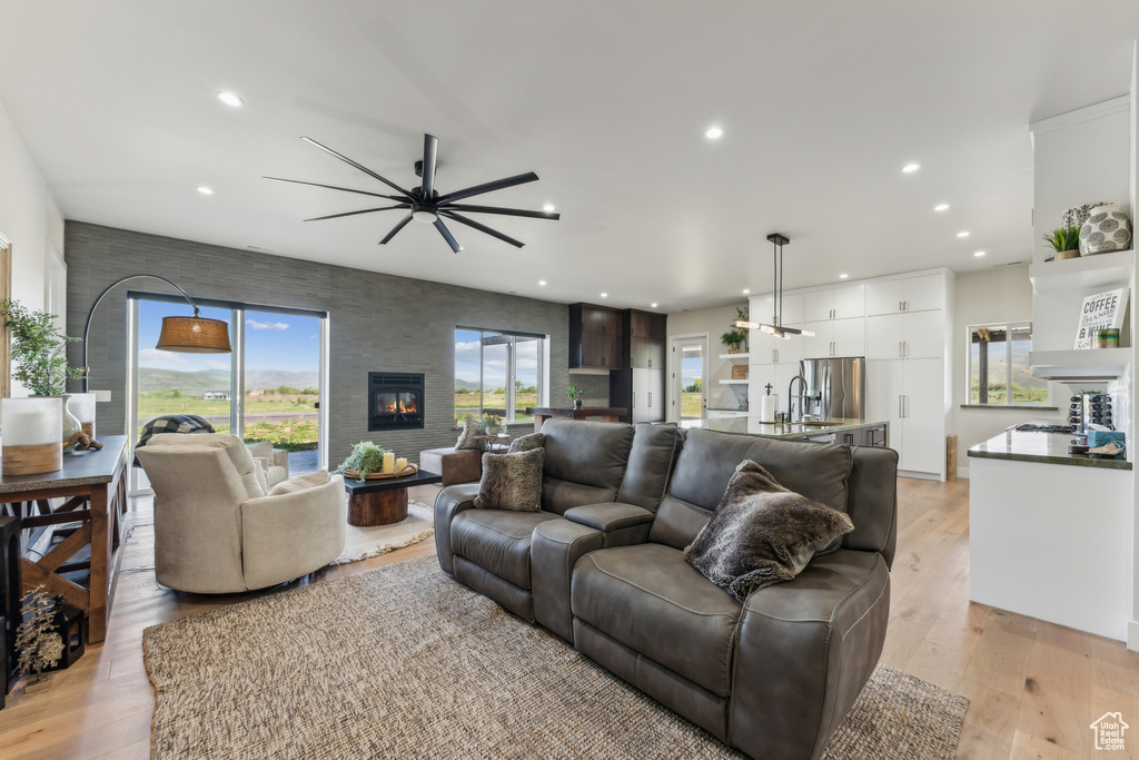 Living area featuring a ceiling fan, recessed lighting, a fireplace, and light wood-style flooring