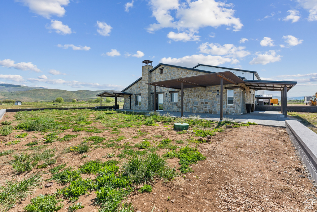 Rear view of property featuring stone siding, a chimney, a patio, and a mountain view