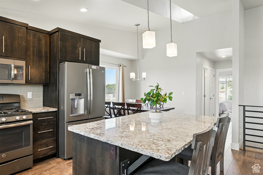 Kitchen with appliances with stainless steel finishes, a breakfast bar area, wood finished floors, dark brown cabinetry, and recessed lighting