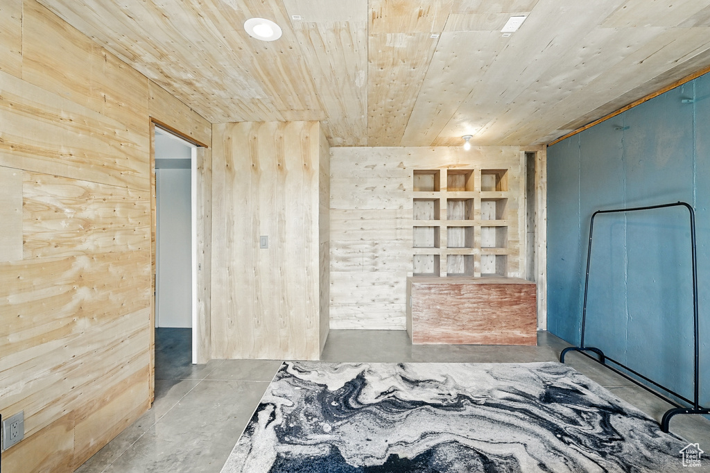 Unfurnished bedroom with concrete flooring, wood ceiling, and wooden walls