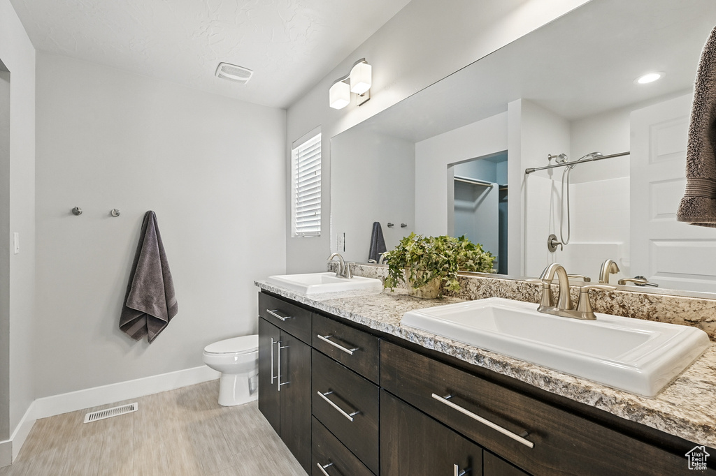 Bathroom with double vanity, wood finished floors, baseboards, toilet, and a shower