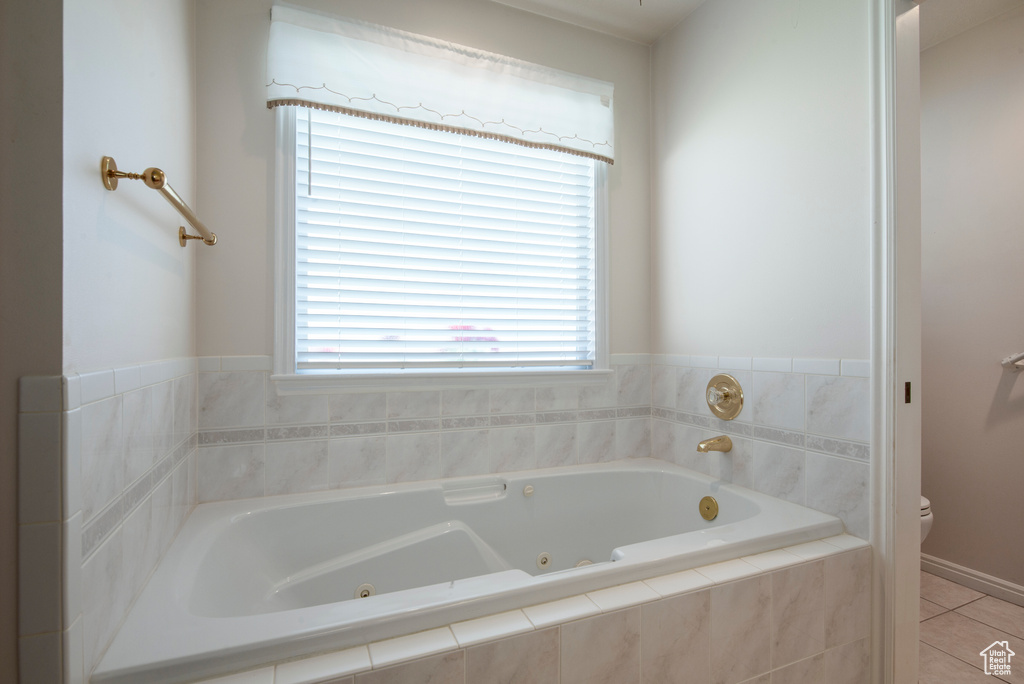 Bathroom with toilet, a jetted tub, and tile patterned flooring