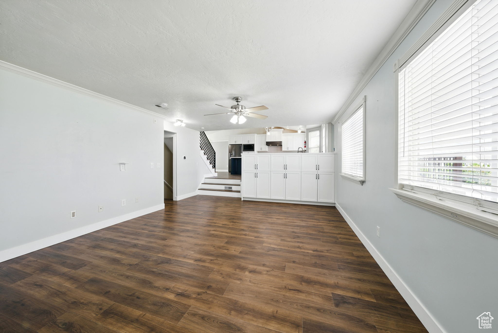 Unfurnished living room with stairs, baseboards, a ceiling fan, dark wood-style floors, and crown molding