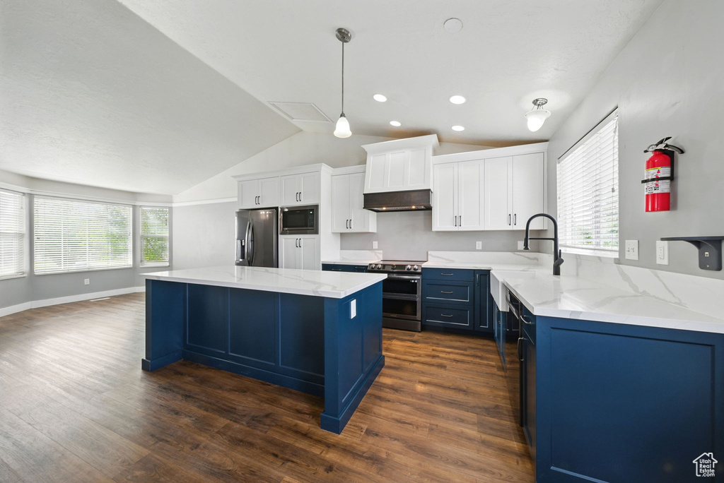 Kitchen with appliances with stainless steel finishes, blue cabinetry, lofted ceiling, range hood, and dark wood-style floors