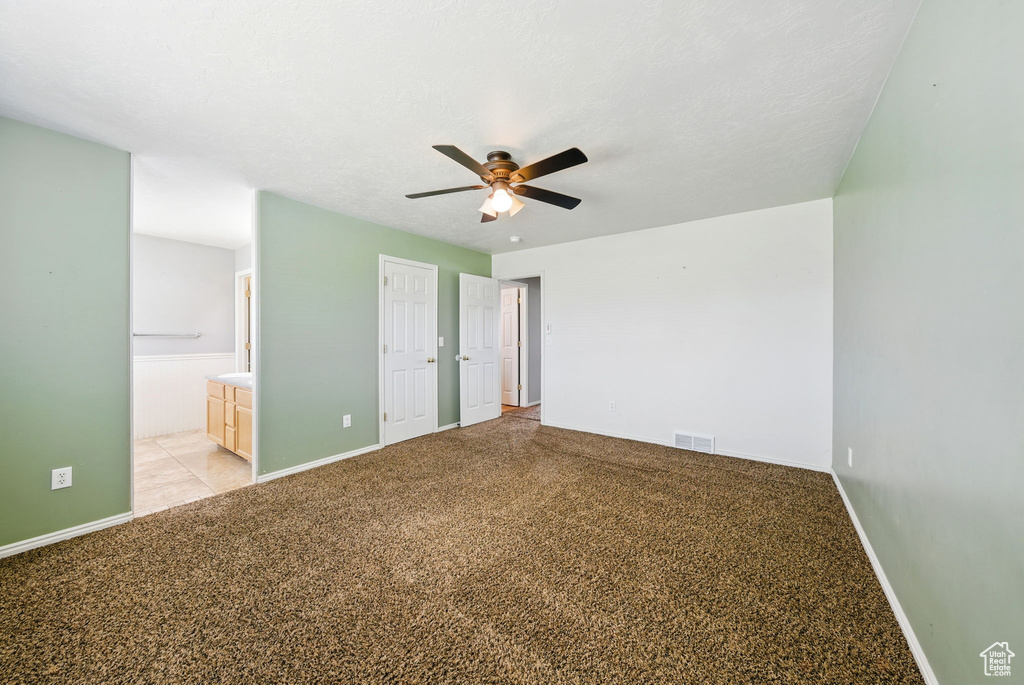 Unfurnished bedroom featuring baseboards, light colored carpet, ensuite bath, and a ceiling fan