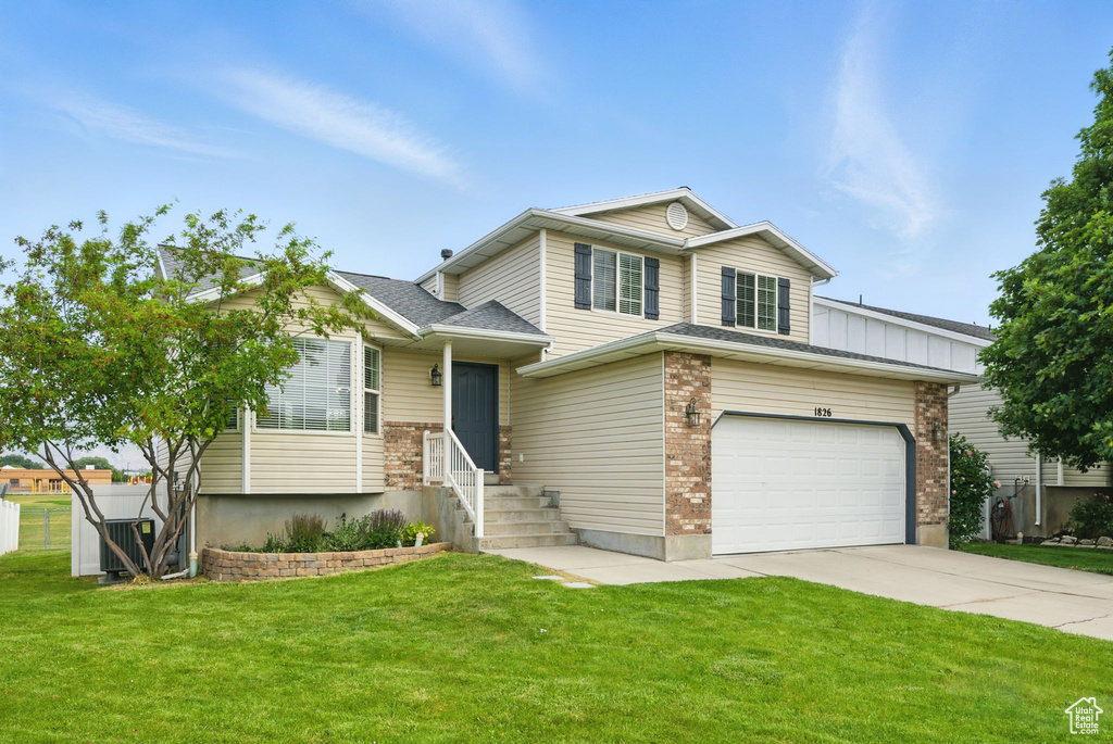 Split level home with concrete driveway, a front yard, a garage, and brick siding