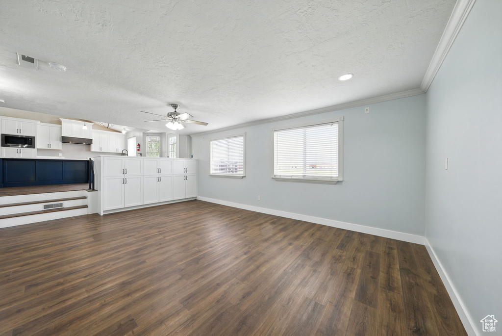Unfurnished living room featuring baseboards, a textured ceiling, dark wood finished floors, ceiling fan, and ornamental molding