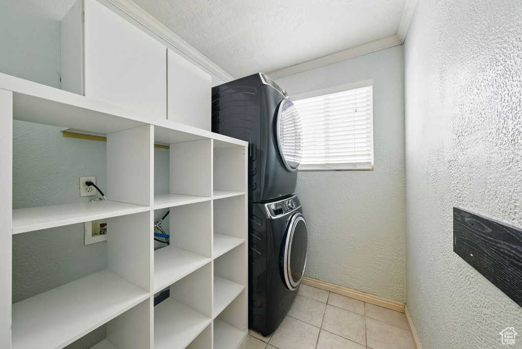 Washroom featuring stacked washer and clothes dryer, baseboards, ornamental molding, light tile patterned flooring, and a textured wall