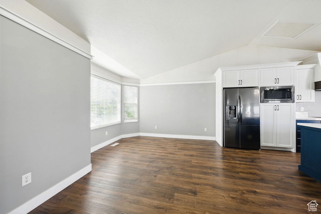 Kitchen featuring fridge with ice dispenser, stainless steel microwave, vaulted ceiling, white cabinetry, and dark wood-style floors