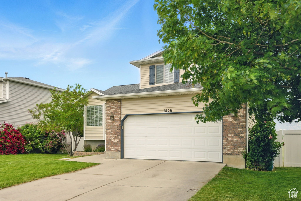 View of front of house featuring concrete driveway, brick siding, a front lawn, and a garage