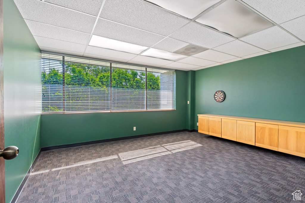 Carpeted empty room featuring a drop ceiling and baseboards