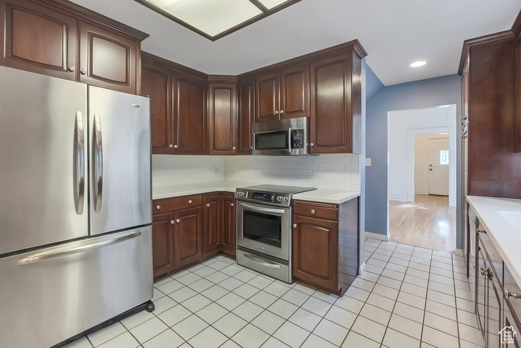Kitchen with stainless steel appliances, light countertops, backsplash, light tile patterned floors, and recessed lighting