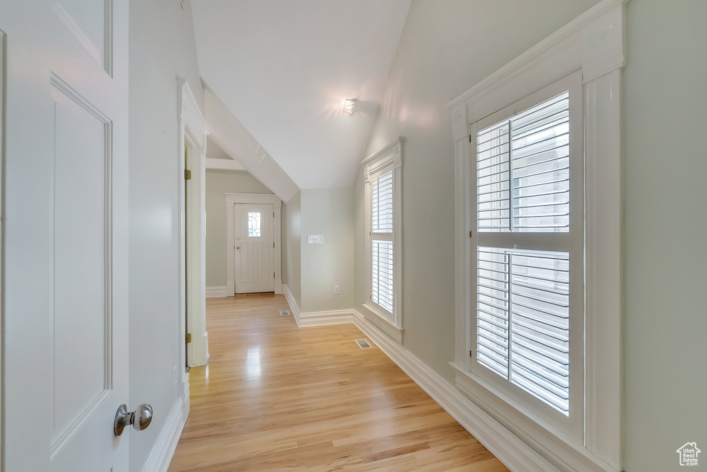 Hall featuring light wood-style floors, baseboards, and lofted ceiling