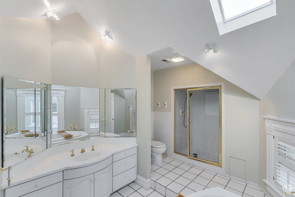 Full bath featuring toilet, lofted ceiling, vanity, a stall shower, and a skylight
