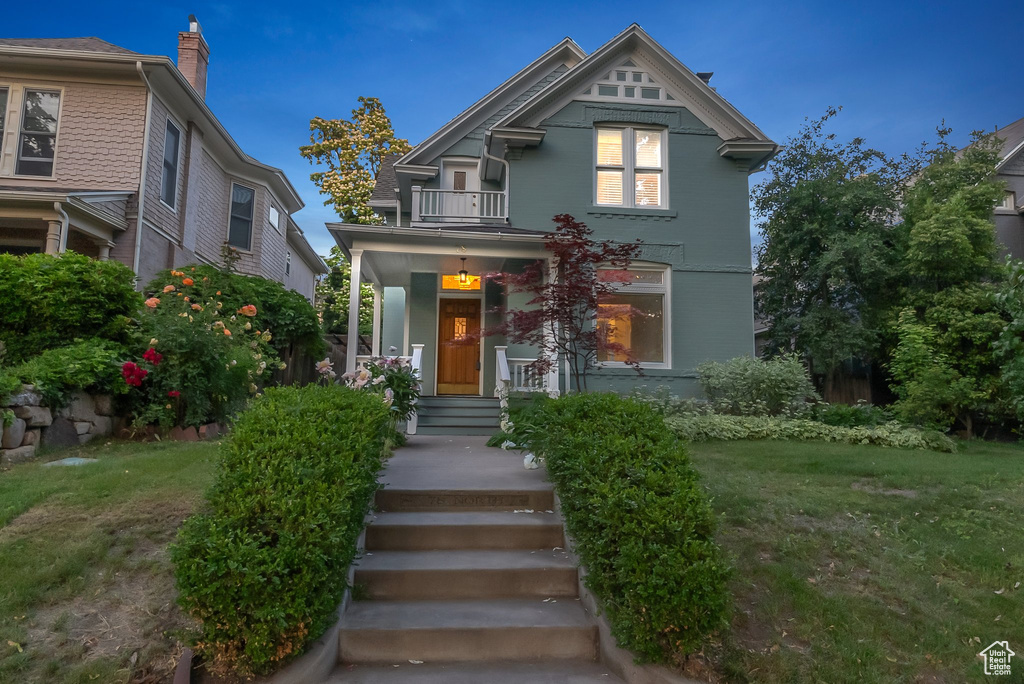 Victorian-style house with a balcony, a chimney, and a front yard