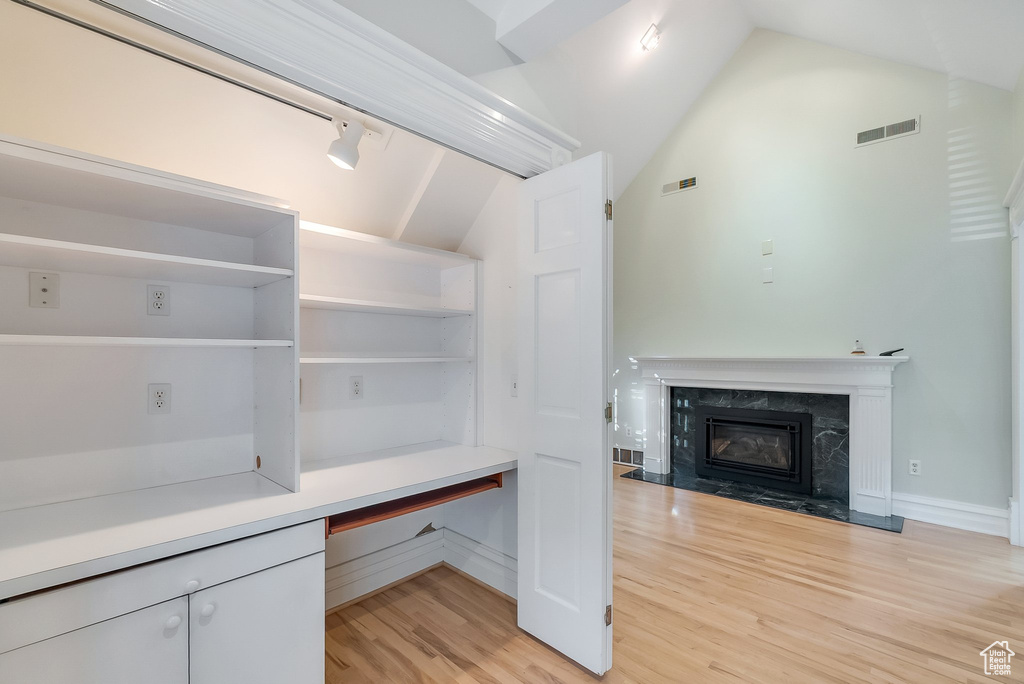 Unfurnished office featuring light wood-style flooring, vaulted ceiling, a fireplace, and baseboards
