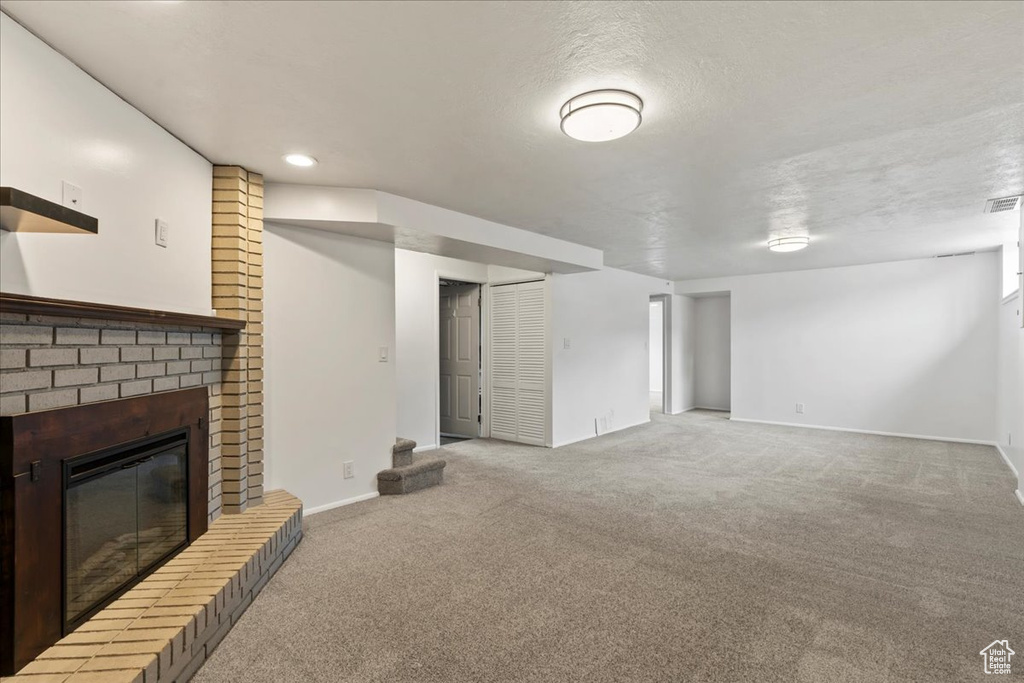 Unfurnished living room featuring carpet, a fireplace, baseboards, recessed lighting, and a textured ceiling