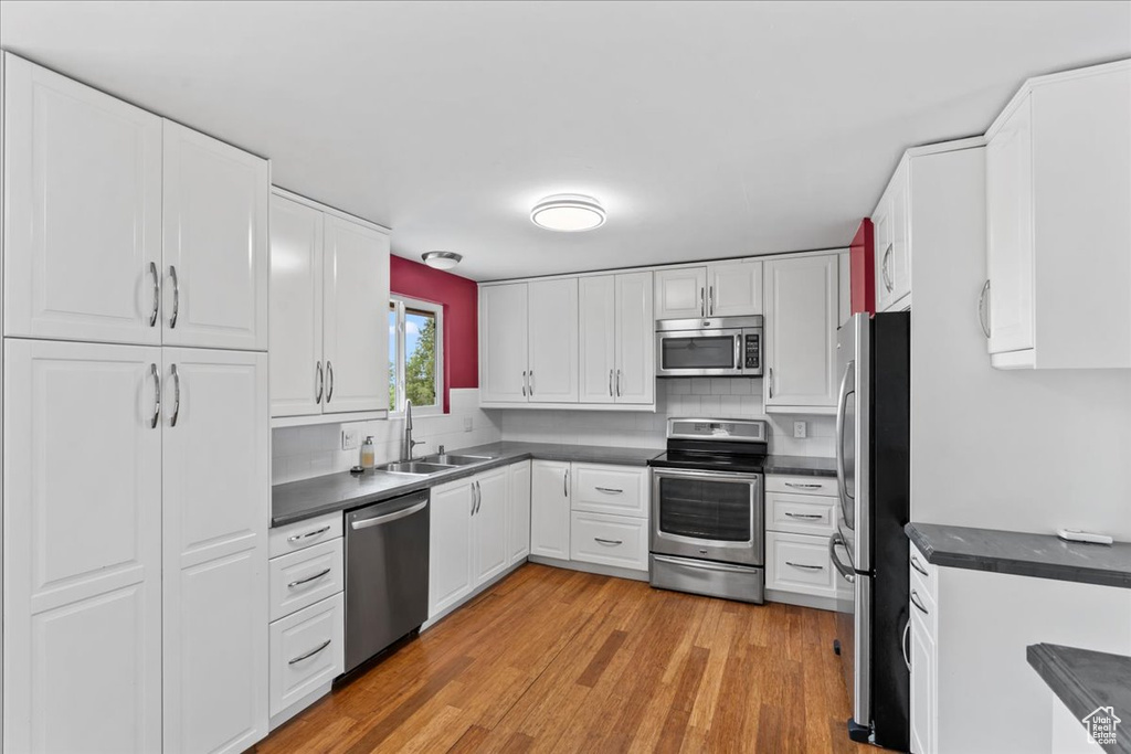 Kitchen featuring appliances with stainless steel finishes, dark countertops, a sink, white cabinetry, and light wood-style flooring