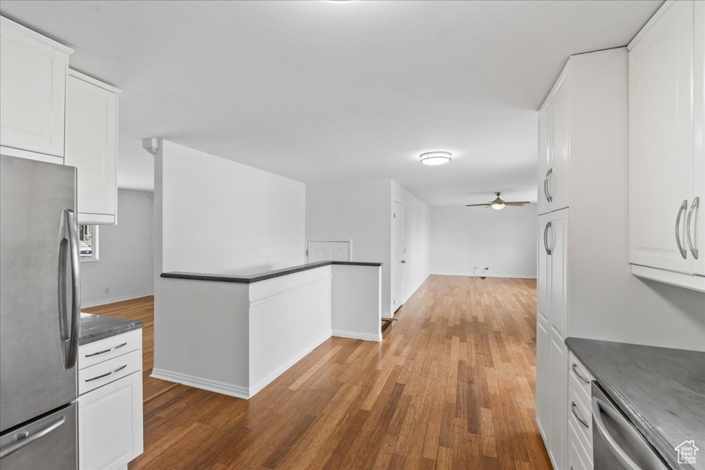 Kitchen featuring appliances with stainless steel finishes, dark countertops, ceiling fan, wood finished floors, and white cabinetry