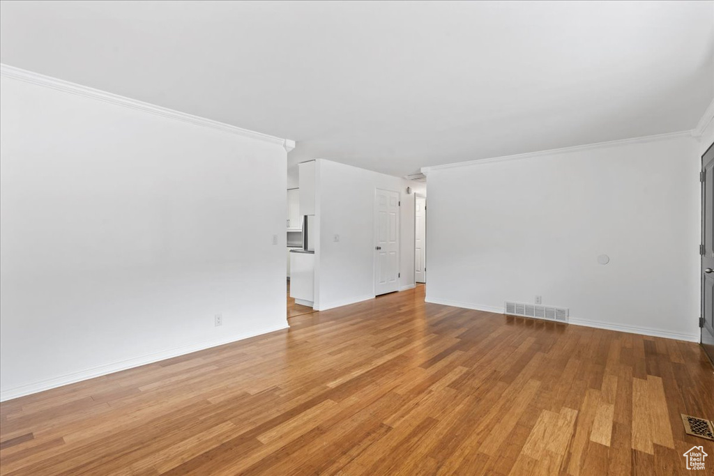 Empty room featuring light wood-style floors, crown molding, and baseboards