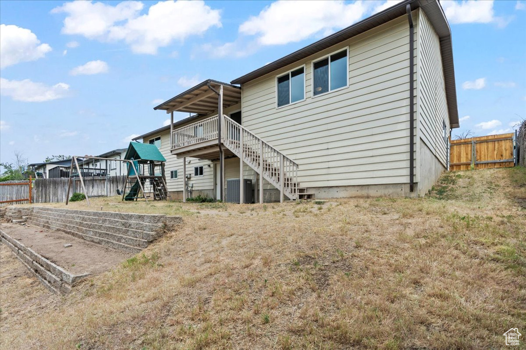 Rear view of house featuring a playground, central air condition unit, a wooden deck, and stairway