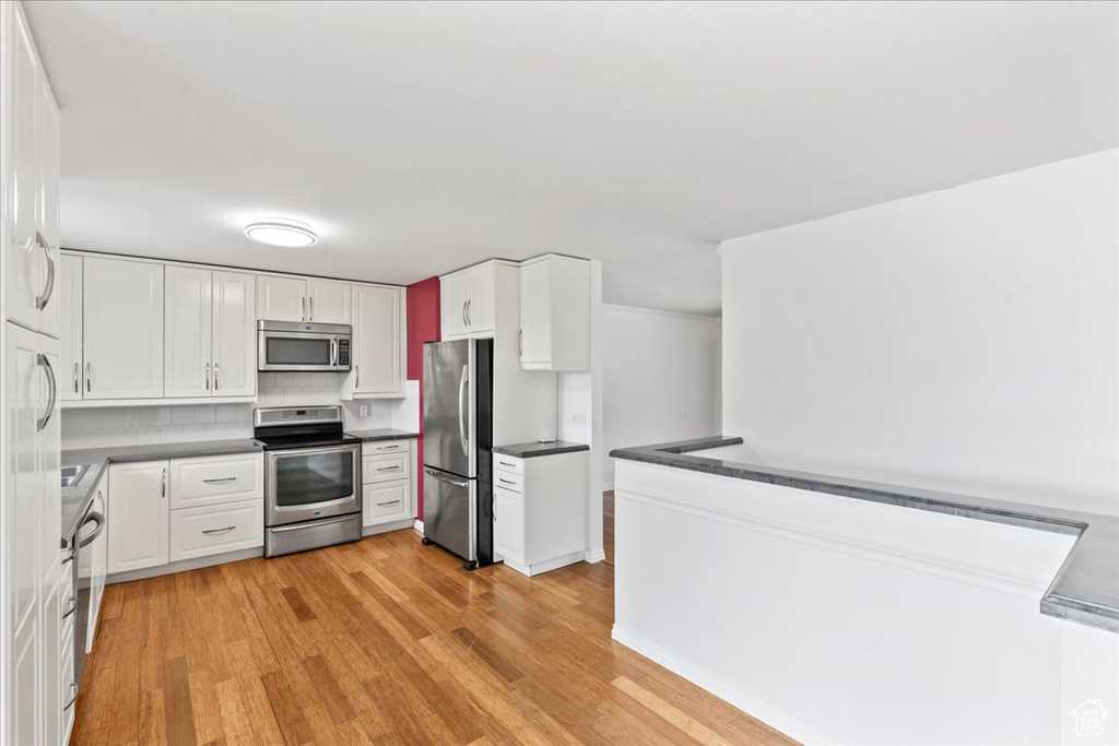 Kitchen with stainless steel appliances, light wood-type flooring, dark countertops, and white cabinetry