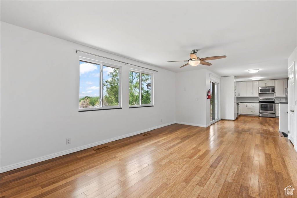 Unfurnished living room with a ceiling fan, light wood finished floors, and baseboards