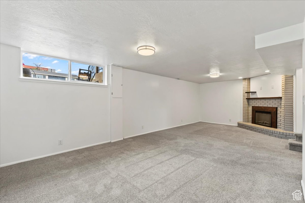 Unfurnished living room featuring a brick fireplace, carpet floors, and baseboards