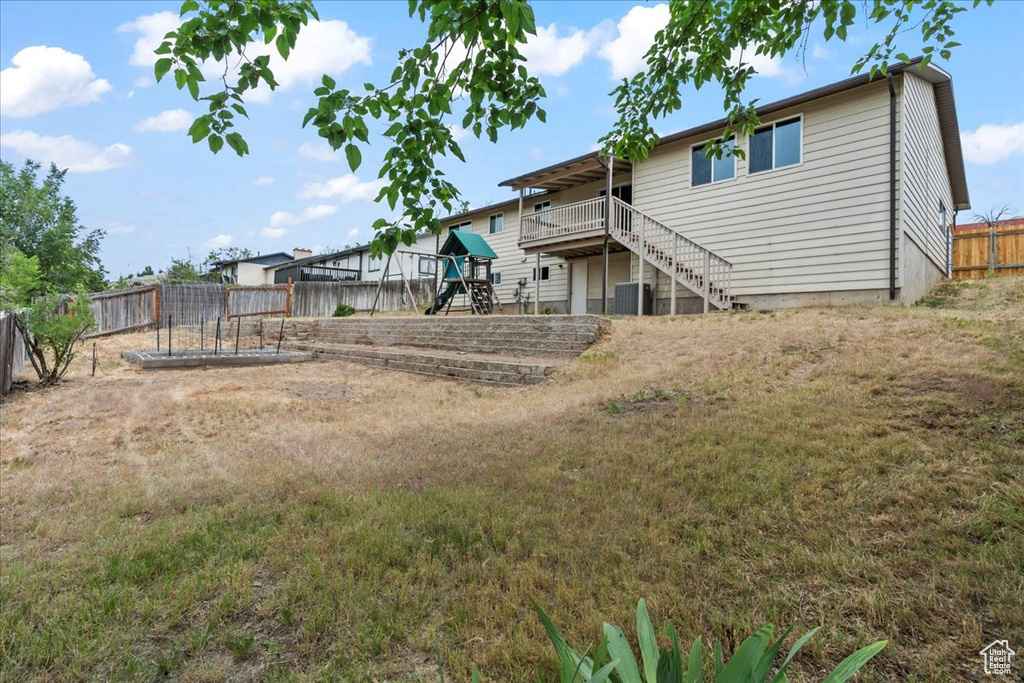 Rear view of house with a playground, stairway, a wooden deck, and central air condition unit
