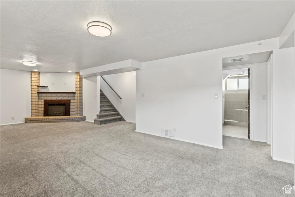 Unfurnished living room with a fireplace, carpet, baseboards, and stairway