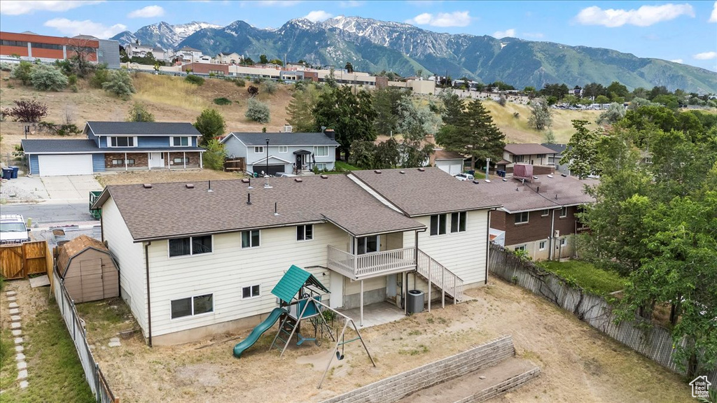 Back of house with a fenced backyard, a mountain view, a shingled roof, and a residential view