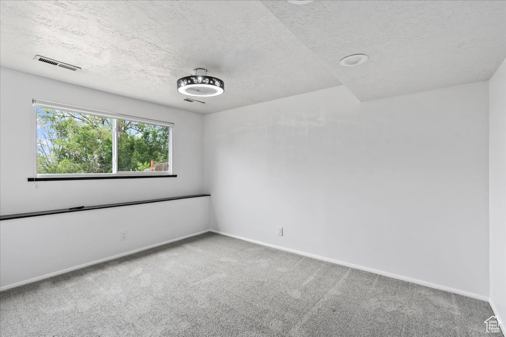 Carpeted empty room with a textured ceiling and baseboards