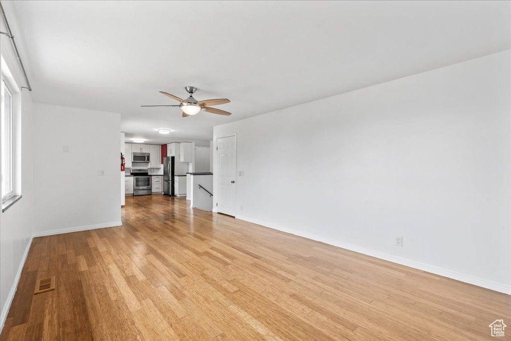 Unfurnished living room featuring baseboards, ceiling fan, and light wood-type flooring