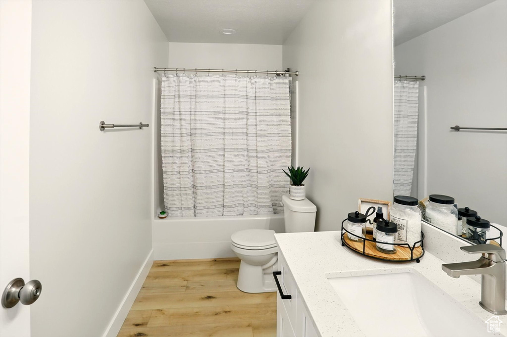 Bathroom featuring vanity, wood finished floors, toilet, and shower / bathtub combination with curtain